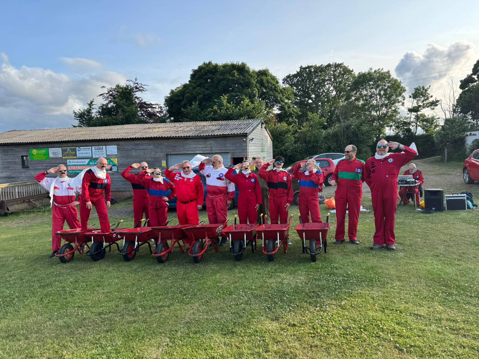 Full team lineup saluting behind red wheelbarrows
